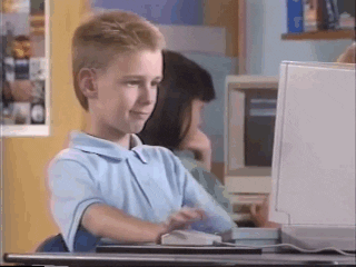 A young boy sitting at a computer, filled with excitement and giving a thumbs up in approval.